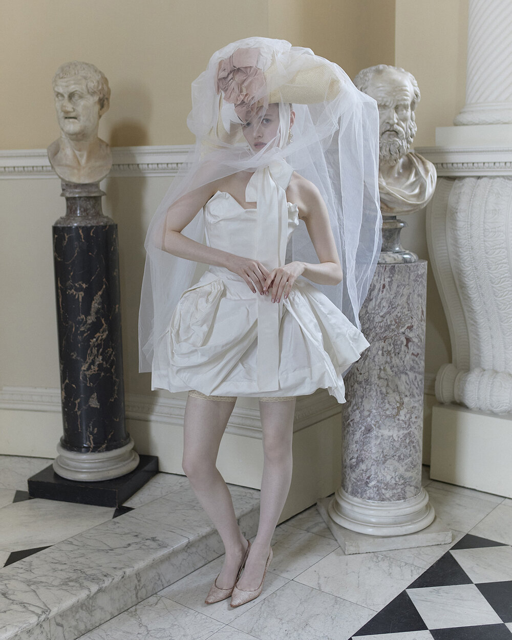 Plot Twist ivory bridal mini with pointed strapless neckline, sculpted draped skirt and a large veiled hat.